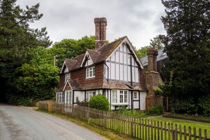 Une maison traditionnelle de style Tudor, caractérisée par une cheminée imposante, une structure en bois peinte en blanc et en noir, et une clôture en bois.