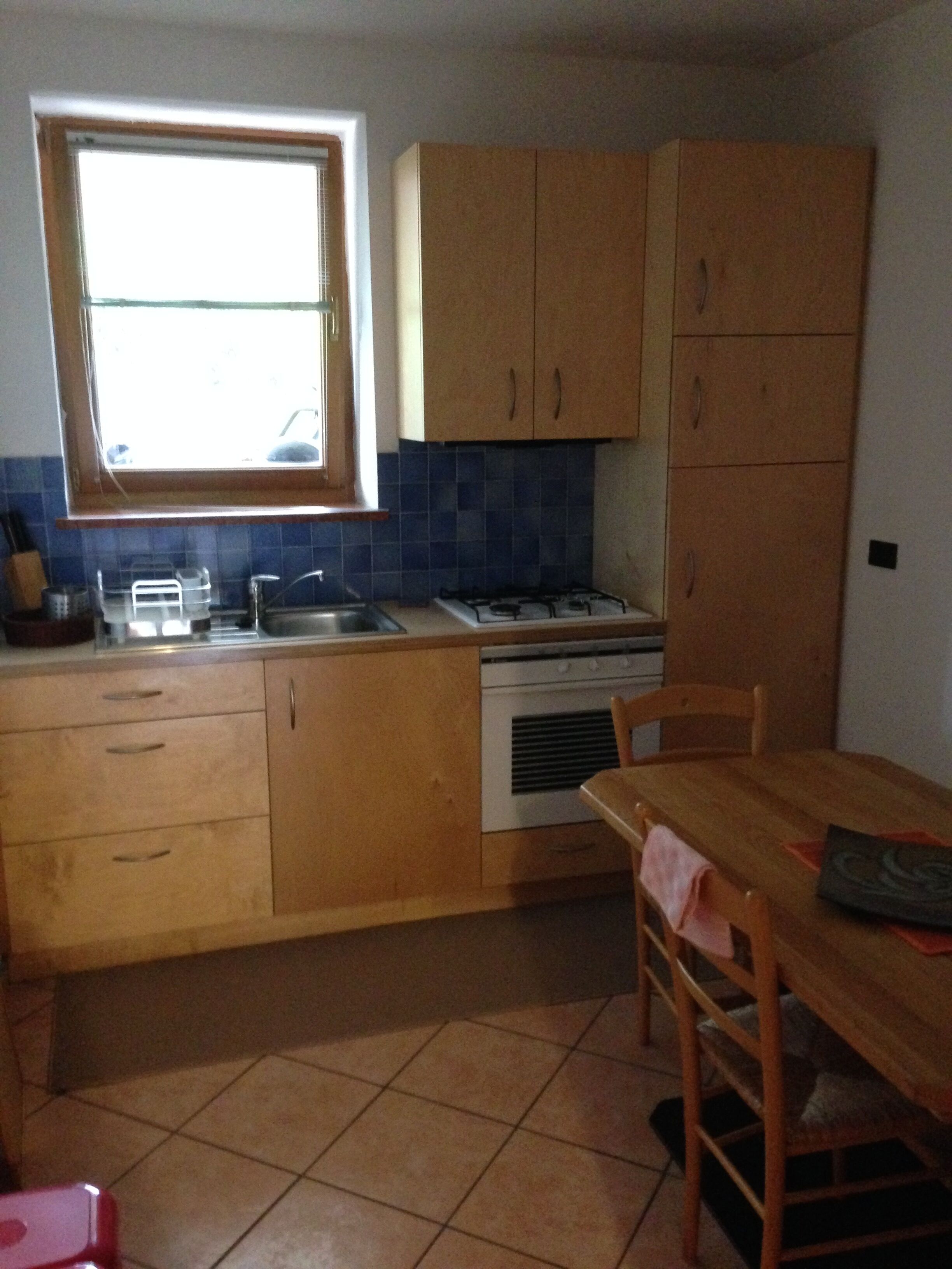 A compact kitchen with wooden cabinets, a gas stove, a sink, and a dining area with a table and chairs.