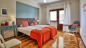 A hotel room with a large bed, two bedside tables, a chair, a window with curtains, and a wooden herringbone floor.