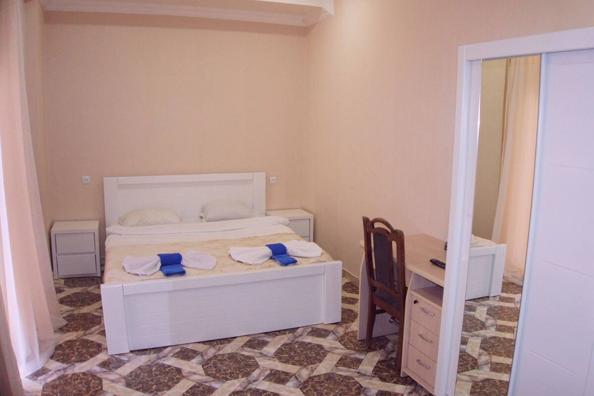 A bedroom with a bed, a nightstand, a desk, and a chair.