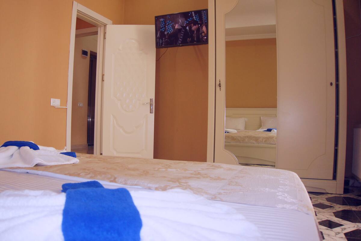 A hotel room with a bed, a bathroom visible through an open door, and a television mounted on the wall.