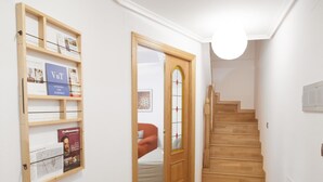 Un couloir avec un escalier en bois, une porte dotée d’un panneau de verre et une étagère fixée au mur, sur laquelle sont posés des magazines.
