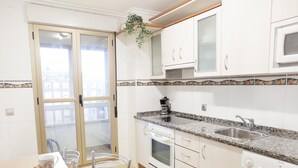 Une cuisine moderne avec des meubles blancs, un plan de travail en granit, un four encastré, un four à micro-ondes, un évier et un lave-linge.
