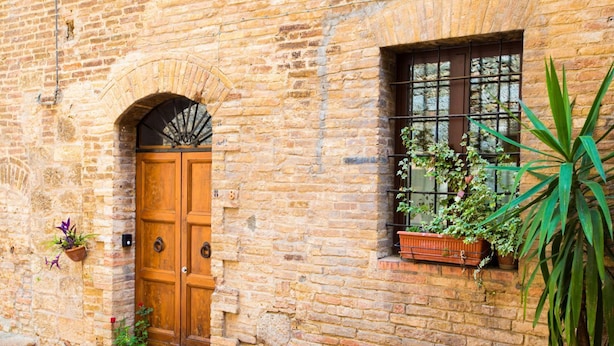 A rustic stone building with a wooden double door, a small window with a metal grid, and potted plants.