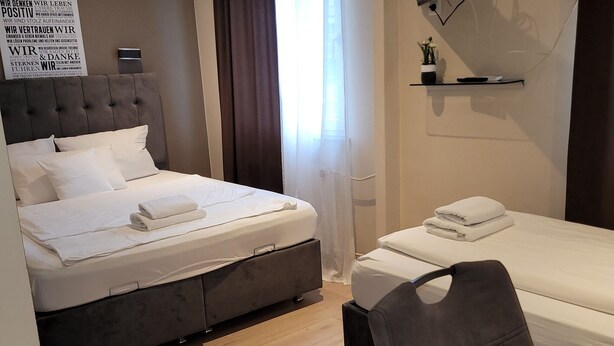A modern hotel room with two beds, a TV mounted on the wall, and a small shelf with a plant. - Hotel Franken an der Messe (Frankfurt)