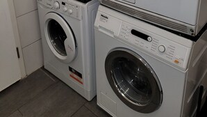 A laundry room with stacked washing machines and dryers. - Hotel Franken an der Messe (Frankfurt)