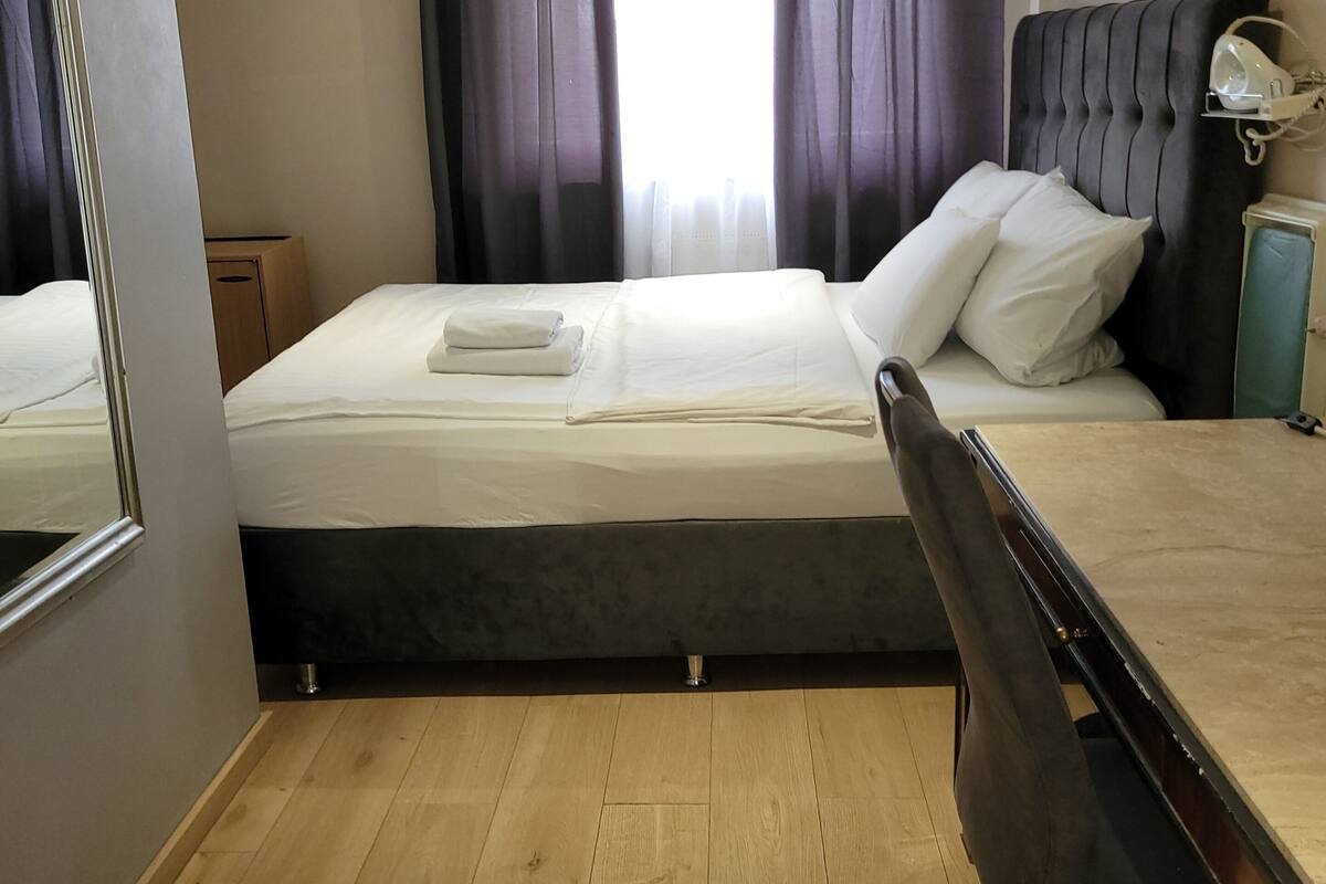 Een hotelkamer met een bed, een bureau, een stoel, een bedlampje en een raam met gordijnen.