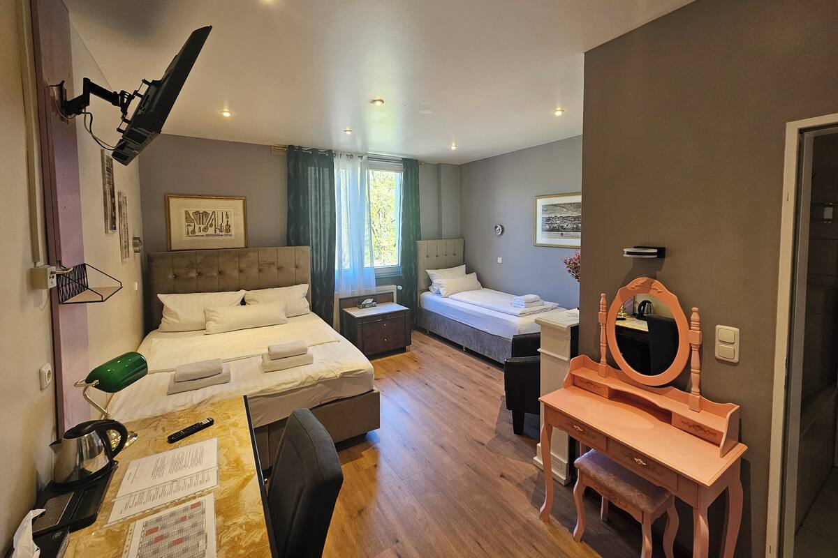 Een hotelkamer met twee bedden, een bureau met stoel, een kaptafel met spiegel en een raam met gordijnen.