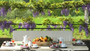 A table set for breakfast with a view of purple wisteria and green foliage. - Stunning private villa for 22 people with A/C, WIFI, private pool, TV, patio and panoramic view (Montebenichi)