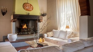 A cozy living room with a fireplace, white furniture, and a vase with branches. - Stunning private villa for 22 people with A/C, WIFI, private pool, TV, patio and panoramic view (Montebenichi)