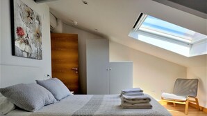 Ein Schlafzimmer mit Dachfenster, einem Bett mit Quiltdecke, einem Sessel und einem Kleiderschrank.