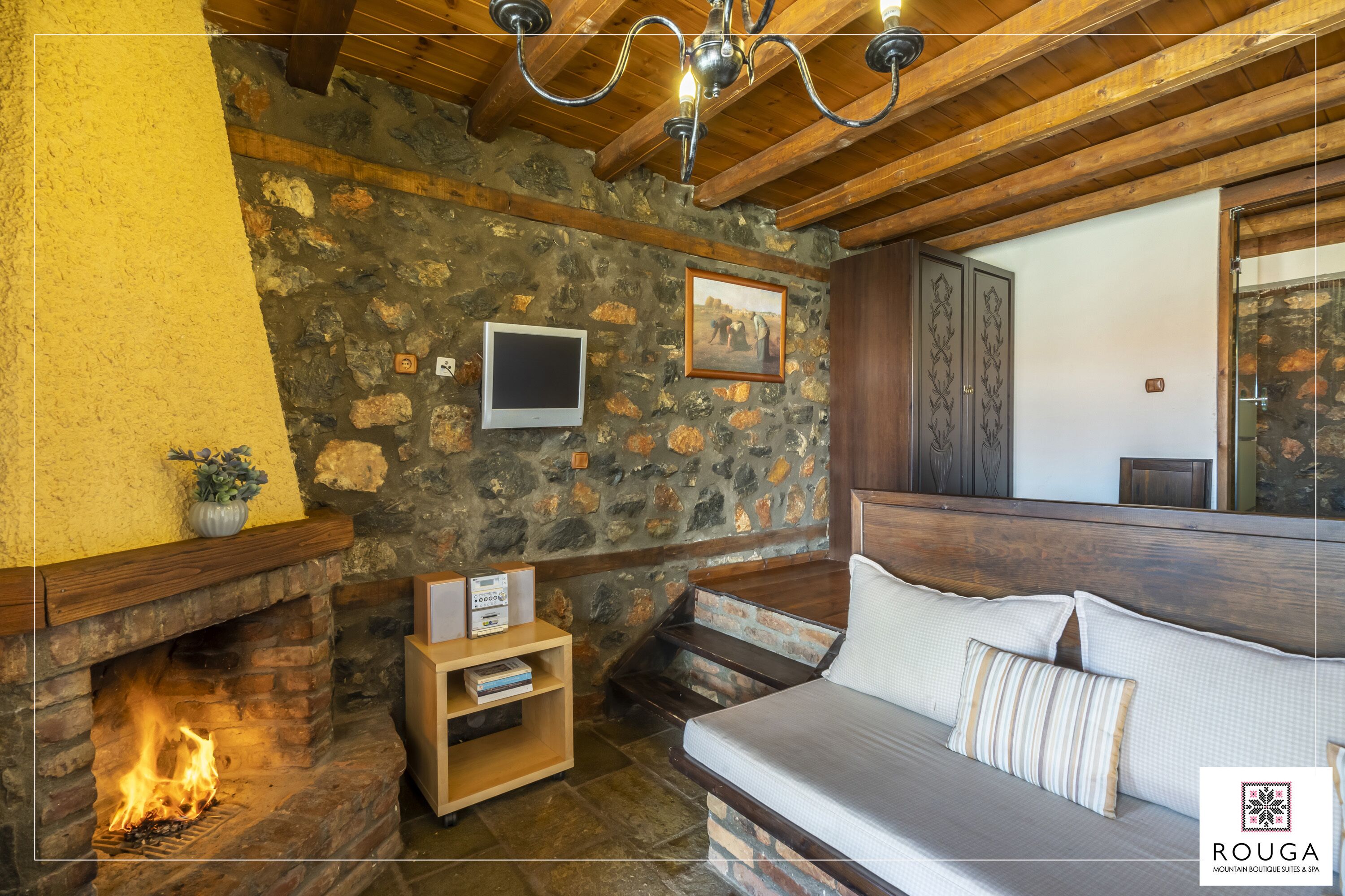 Una habitación acogedora con pared de piedra, chimenea, techo de madera y una cama con almohadas.