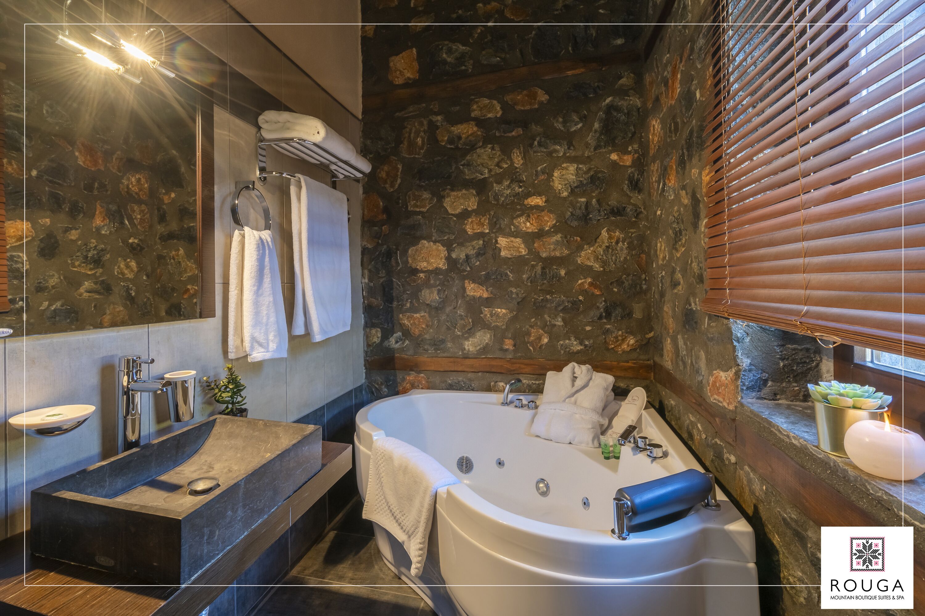 A modern bathroom with a stone wall, a freestanding bathtub, a vanity with a sink, and a towel rack.