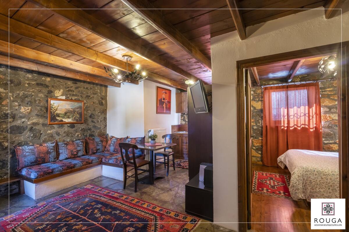 A cozy room with a stone wall, wooden ceiling, a sofa, a dining table, and a bed.