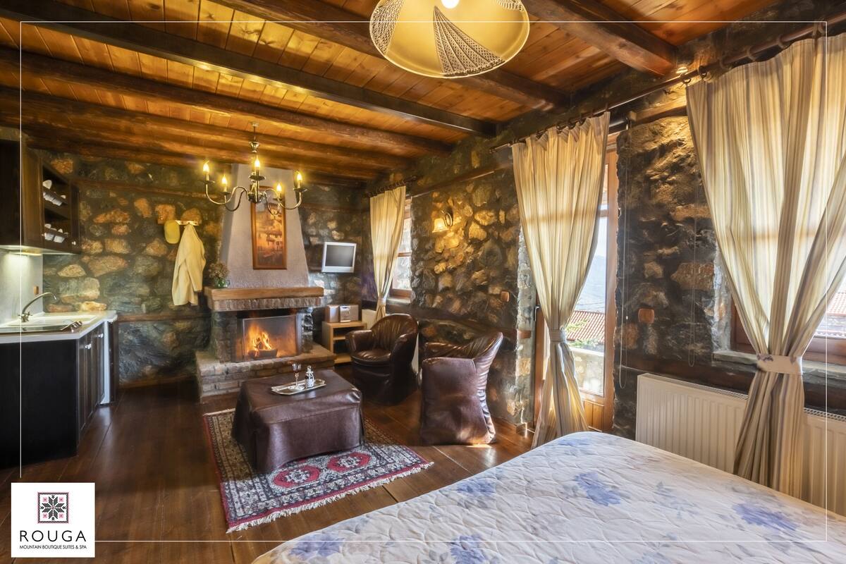 A cozy room with a stone fireplace, wooden ceiling, and a bed with a floral bedspread.