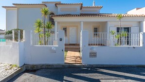 A white two-story house with a tiled roof, a gated entrance, and a small front porch. - Villa Gui by Gabi Miguel (Vale Rebelho)
