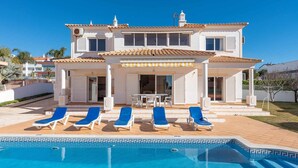 A two-story house with a swimming pool, white exterior, and a covered patio area with blue lounge chairs. - Villa Gui by Gabi Miguel (Vale Rebelho)