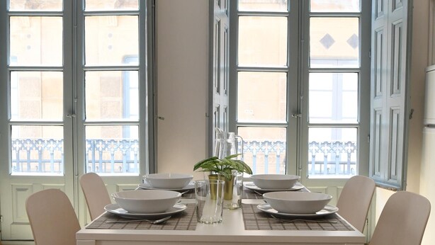 Une table à manger avec quatre chaises, des assiettes blanches, des bols et une carafe d’eau.
