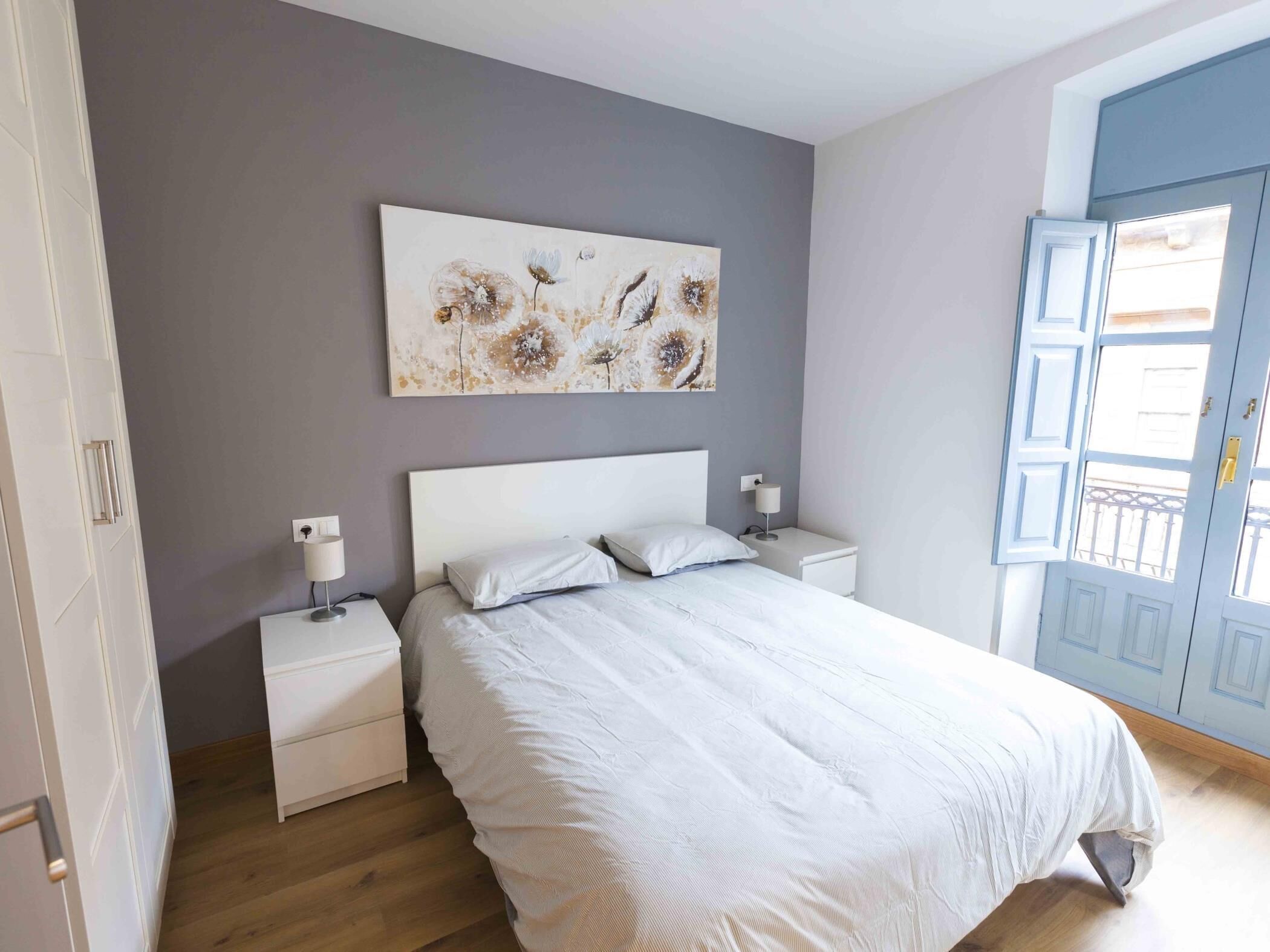 Un dormitorio con cama, mesitas de noche, una obra de arte colgada en la pared y una puerta con vistas.