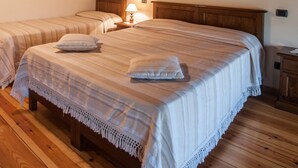 Quarto com duas camas, vigas de madeira, piso de madeira e uma pequena mesa de cabeceira com abajur.