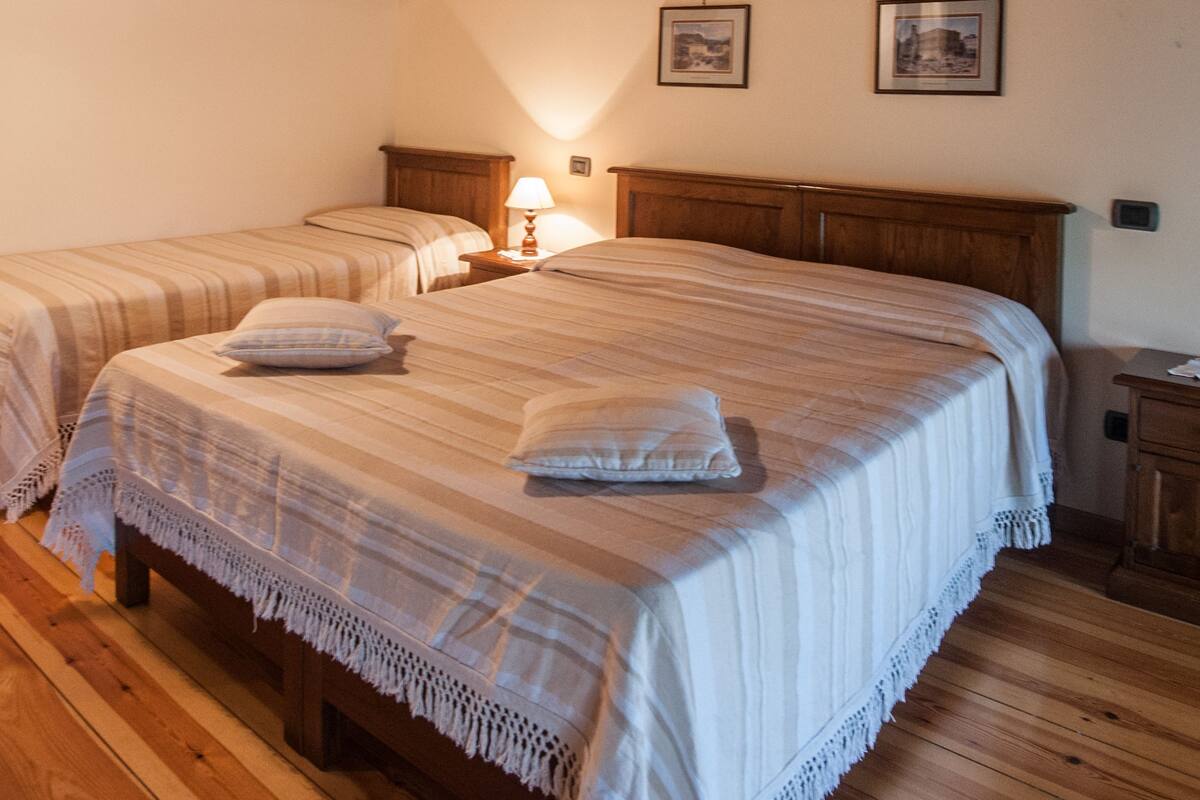 Quarto com duas camas, vigas de madeira, piso de madeira e uma pequena mesa de cabeceira com abajur.