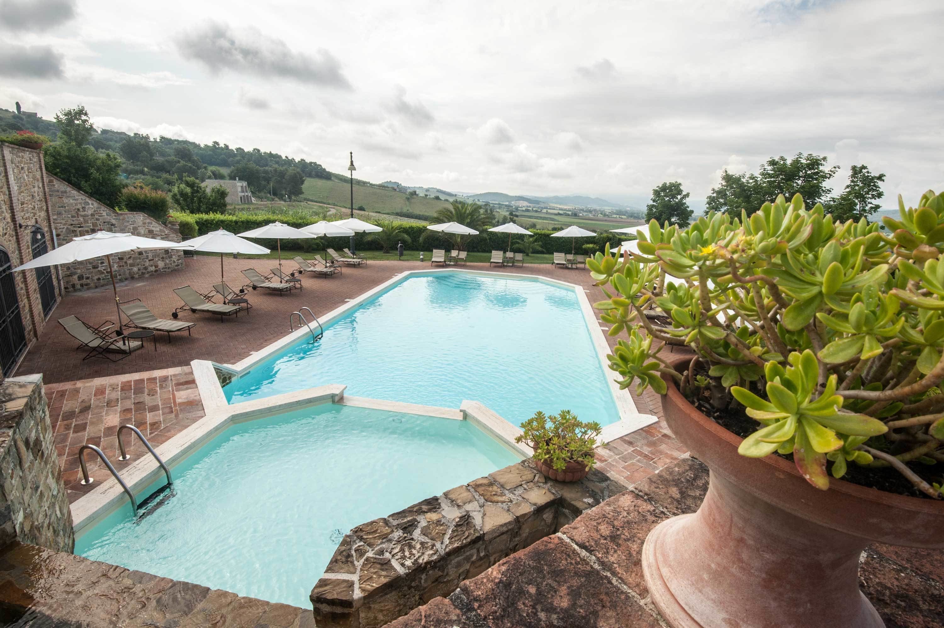 Une piscine entourée de murs en pierre et de plantes en pot, avec des chaises longues et des parasols.