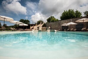A swimming pool with lounge chairs and umbrellas, surrounded by a stone wall and trees. - Casale Giorgio (Magione)