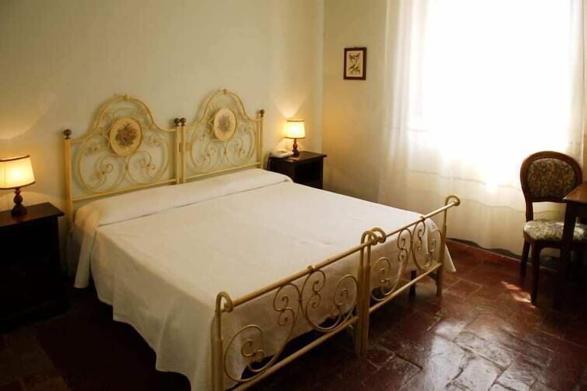 Quarto com cama, duas mesas de cabeceira, uma cadeira e janela com cortinas.