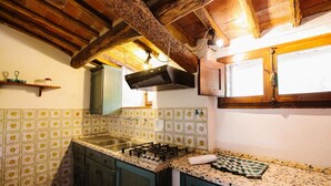 Una cocina con estufa a gas, extractor de humos colgante y ventana con marco de madera.