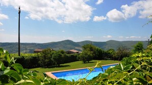 Piscina rodeada de vegetación, con vistas a colinas distantes y un cielo despejado.