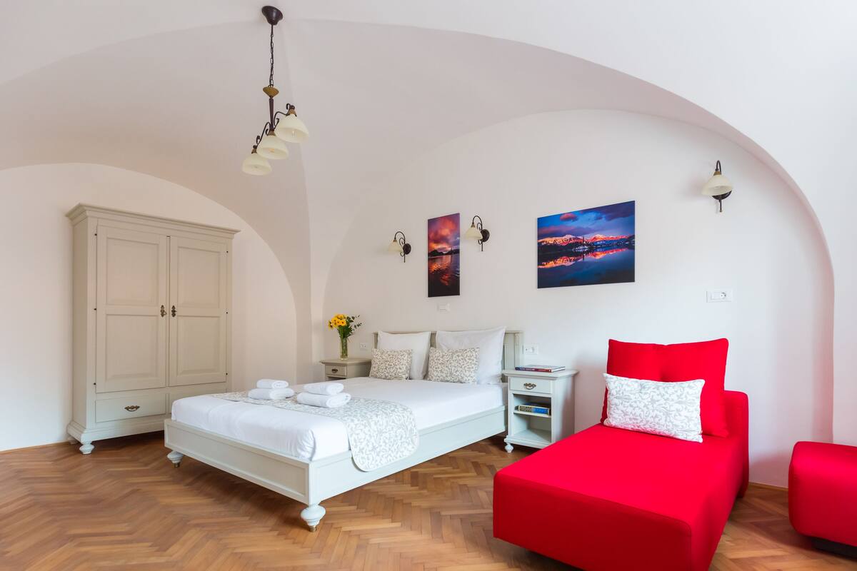A bedroom with a large bed, a red sofa, a wardrobe, and a nightstand.