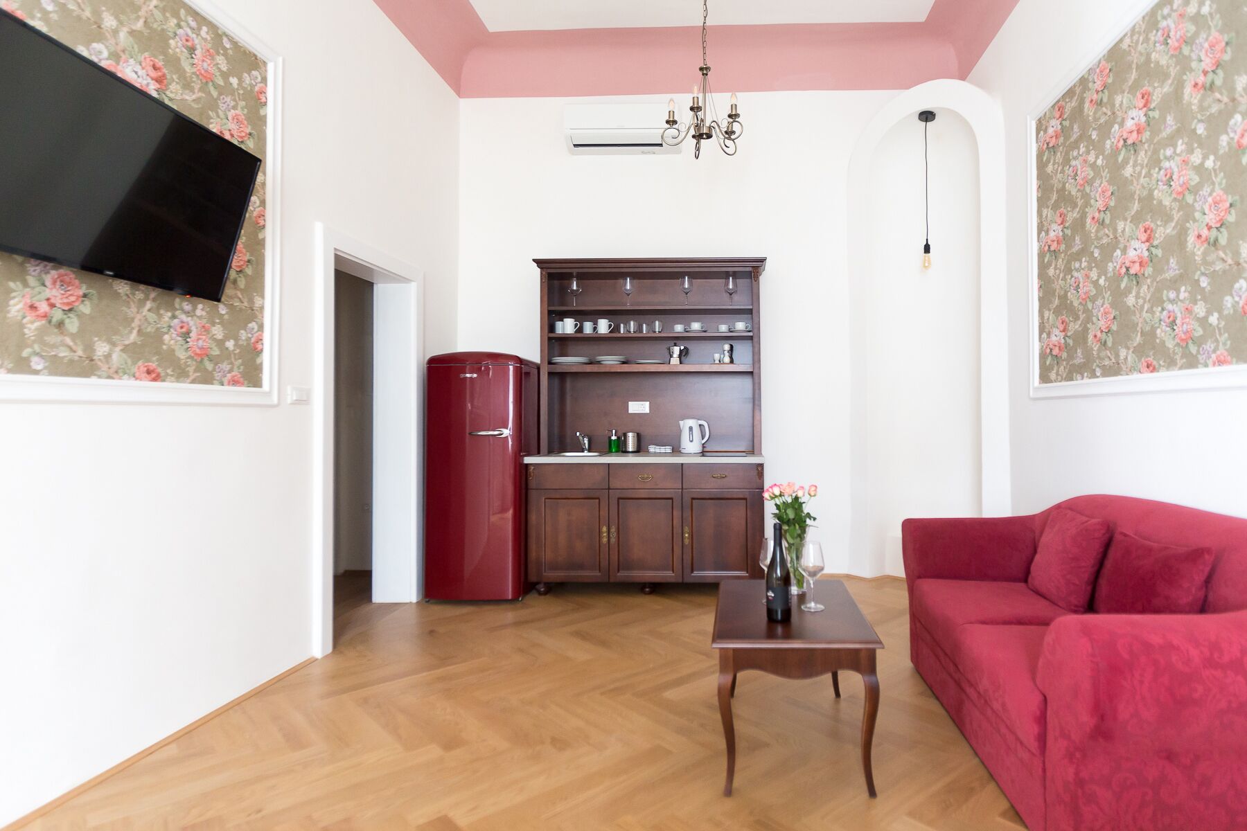 Ein Wohnzimmer mit rotem Sofa, Couchtisch aus Holz und einem an der Wand befestigten Fernseher.