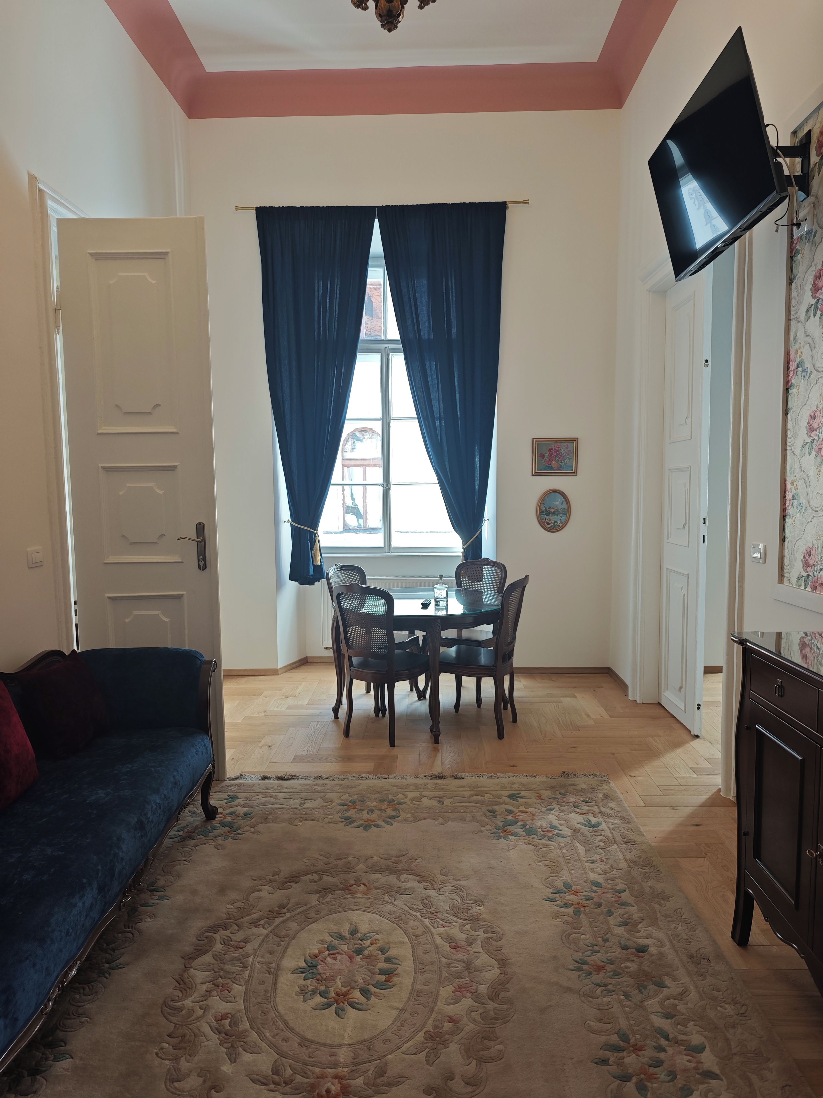 Ein Zimmer mit Esstisch, Stühlen, einer Couch, einem Fernseher und einem gemusterten Teppich.