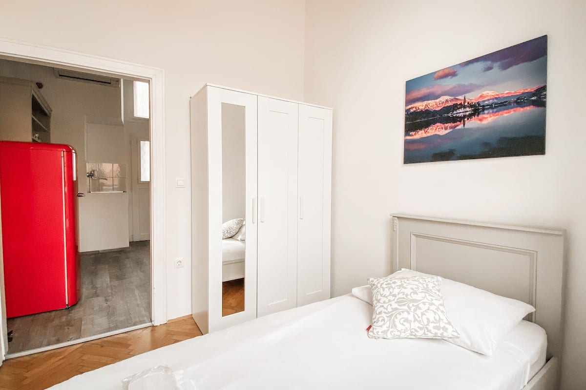 A bedroom with a bed, a white headboard, and a painting of a sunset on the wall.