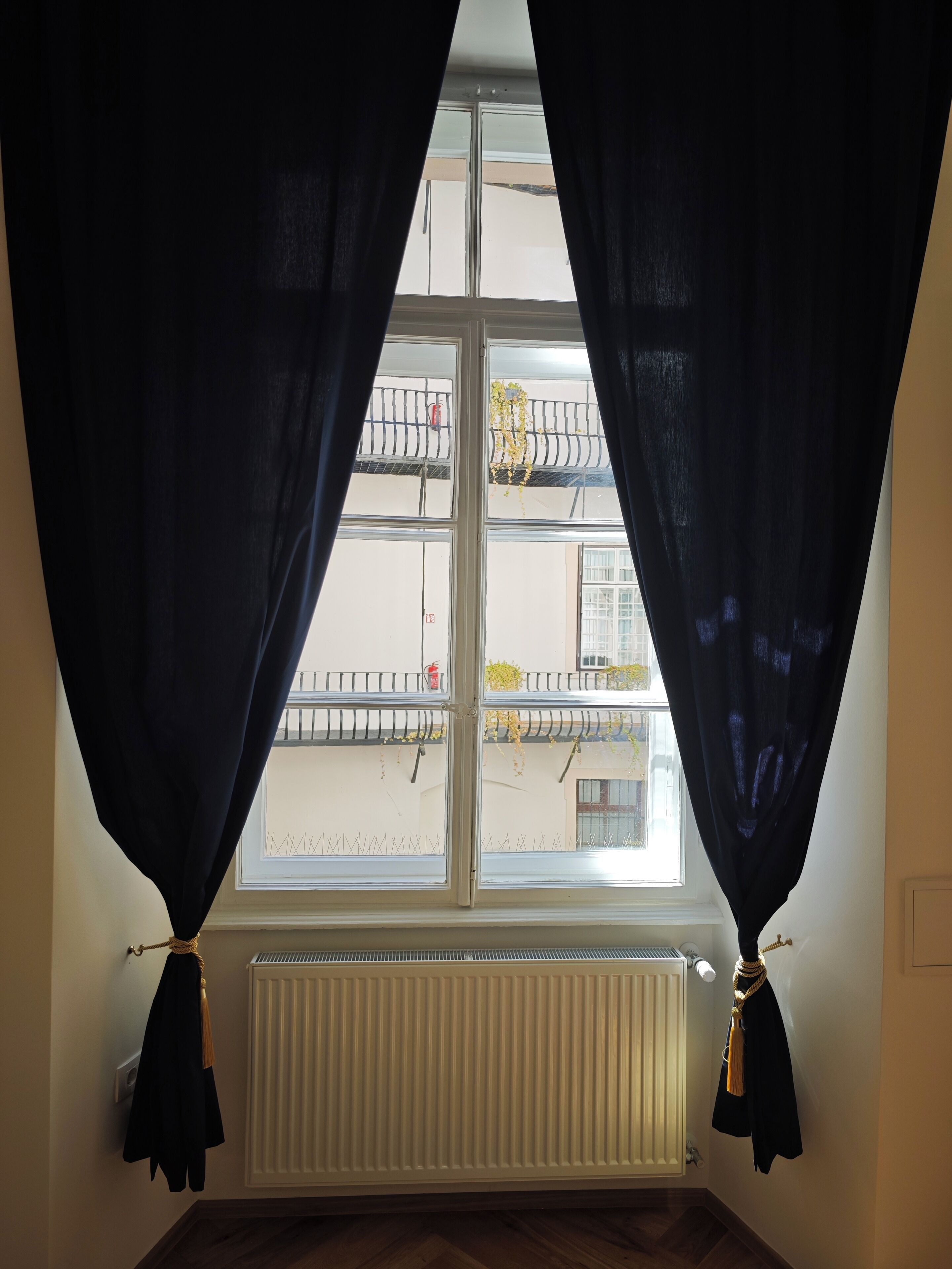 Quarto com janela, radiador branco e cortina preta amarrada à moldura.