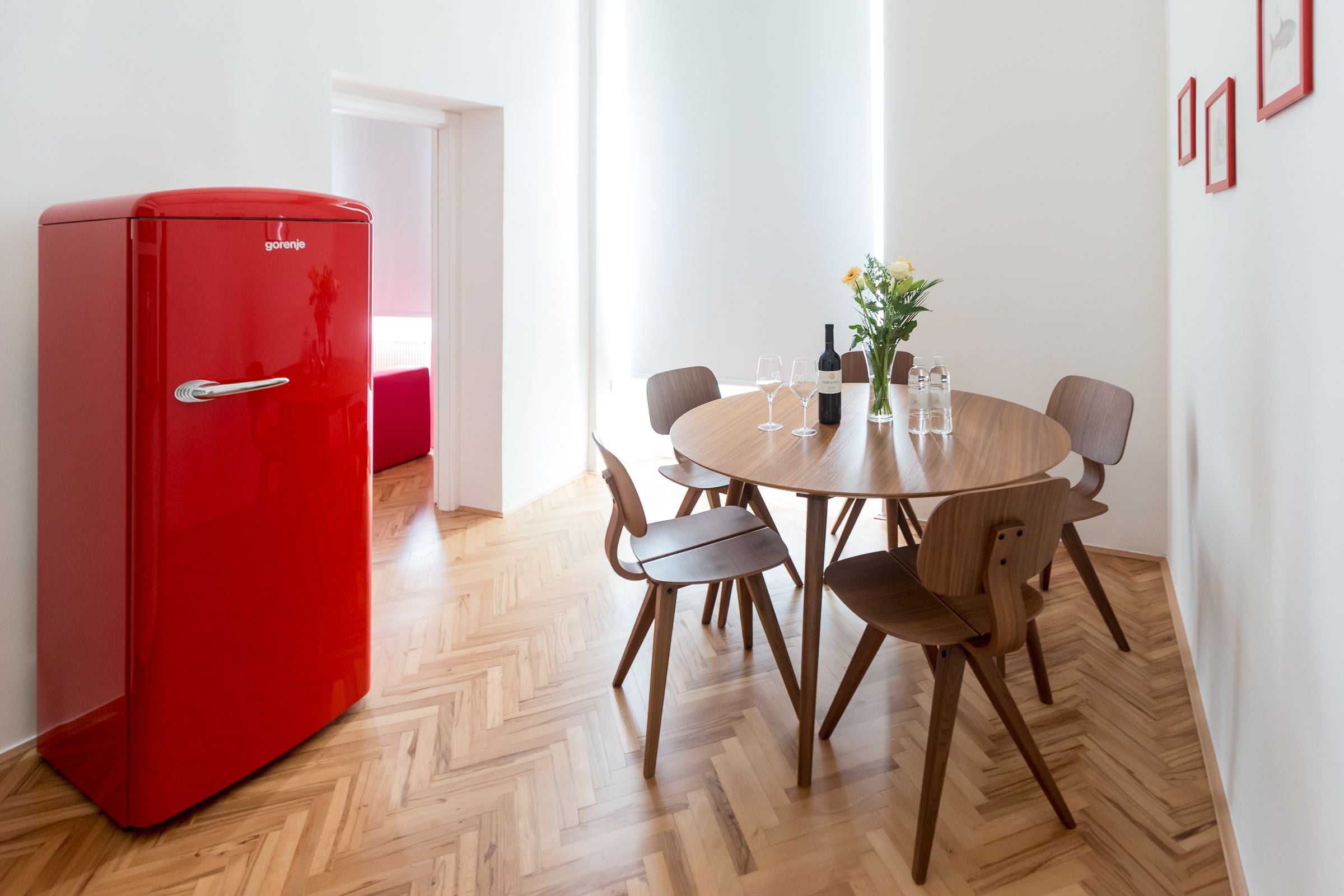 A compact room with a red refrigerator, a wooden dining table with six chairs, and a small potted plant.