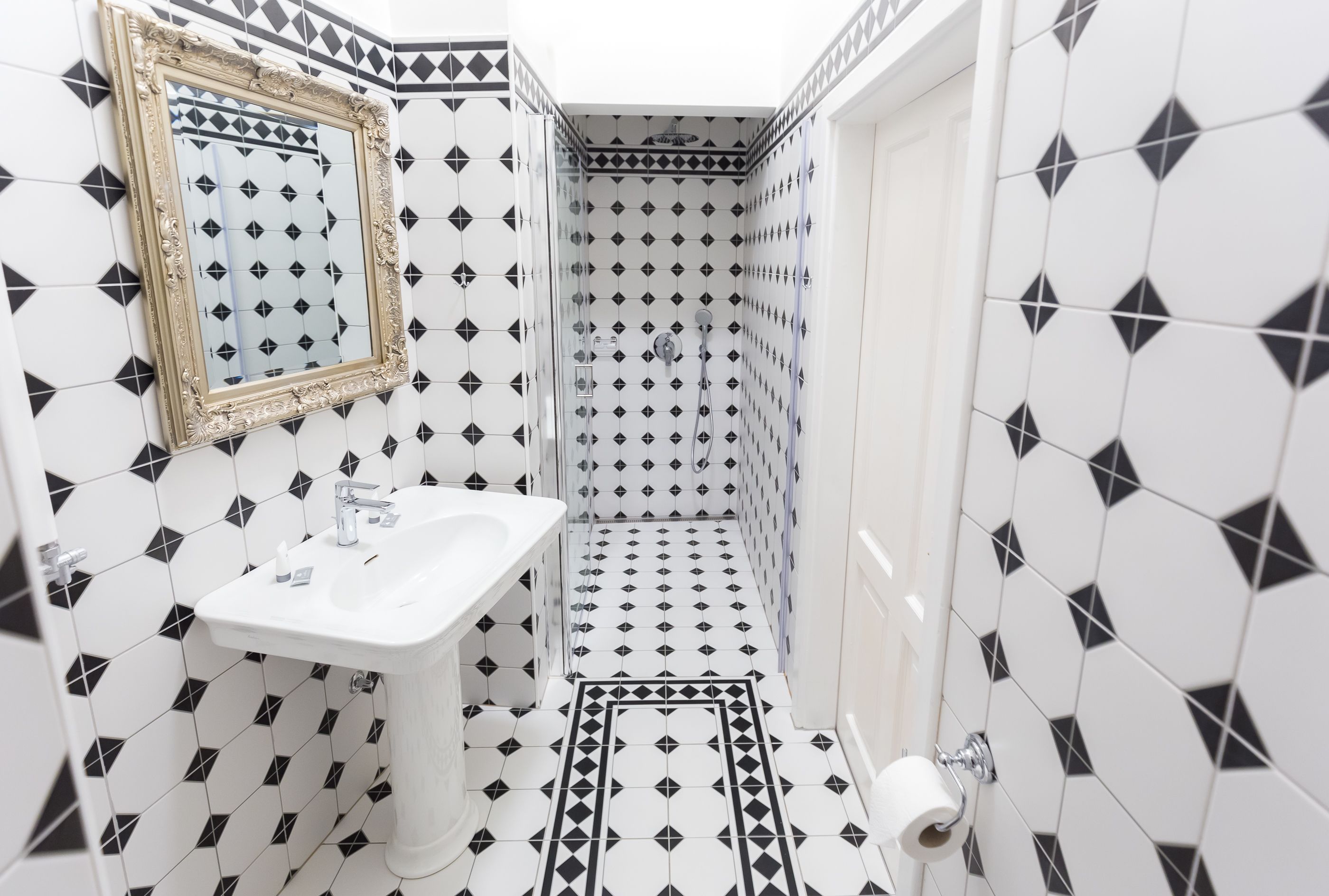 A bathroom with a white sink, a mirror, and black and white patterned tiles.