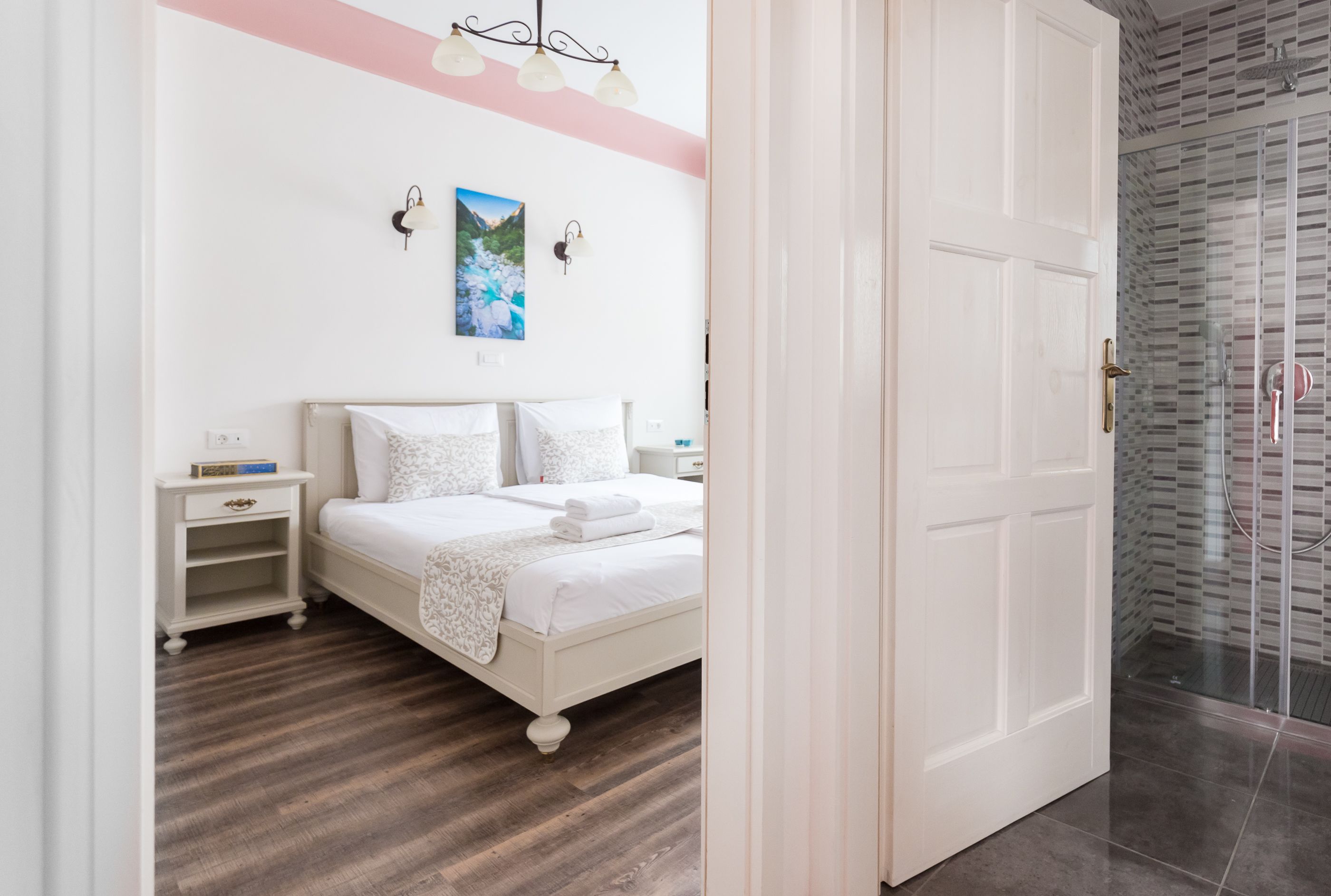 A bedroom with a bed, nightstands, a wall-mounted light fixture, and a door leading to a bathroom with a glass shower.