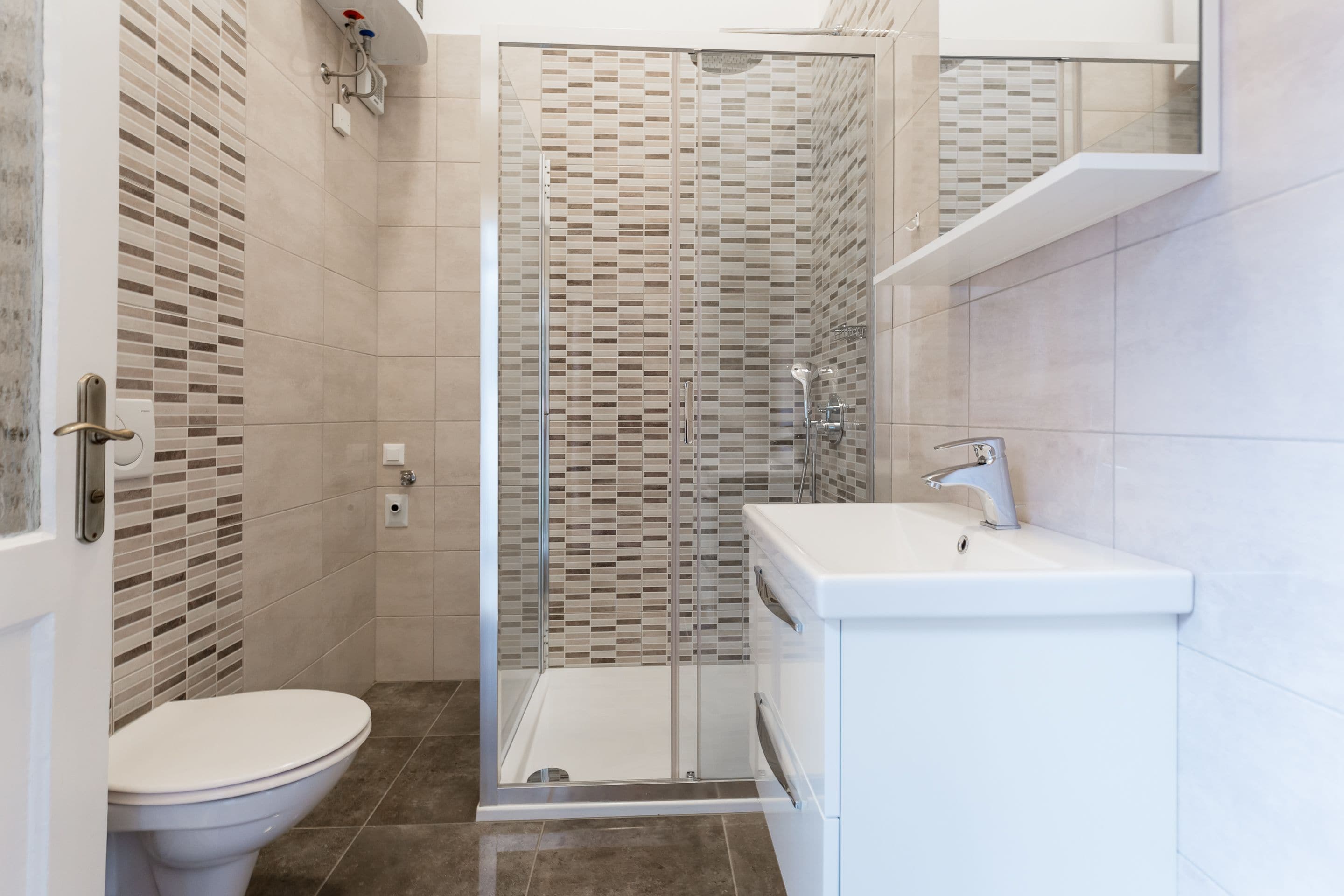 A modern bathroom with a toilet, a shower with a glass door, and a sink with a mirror.