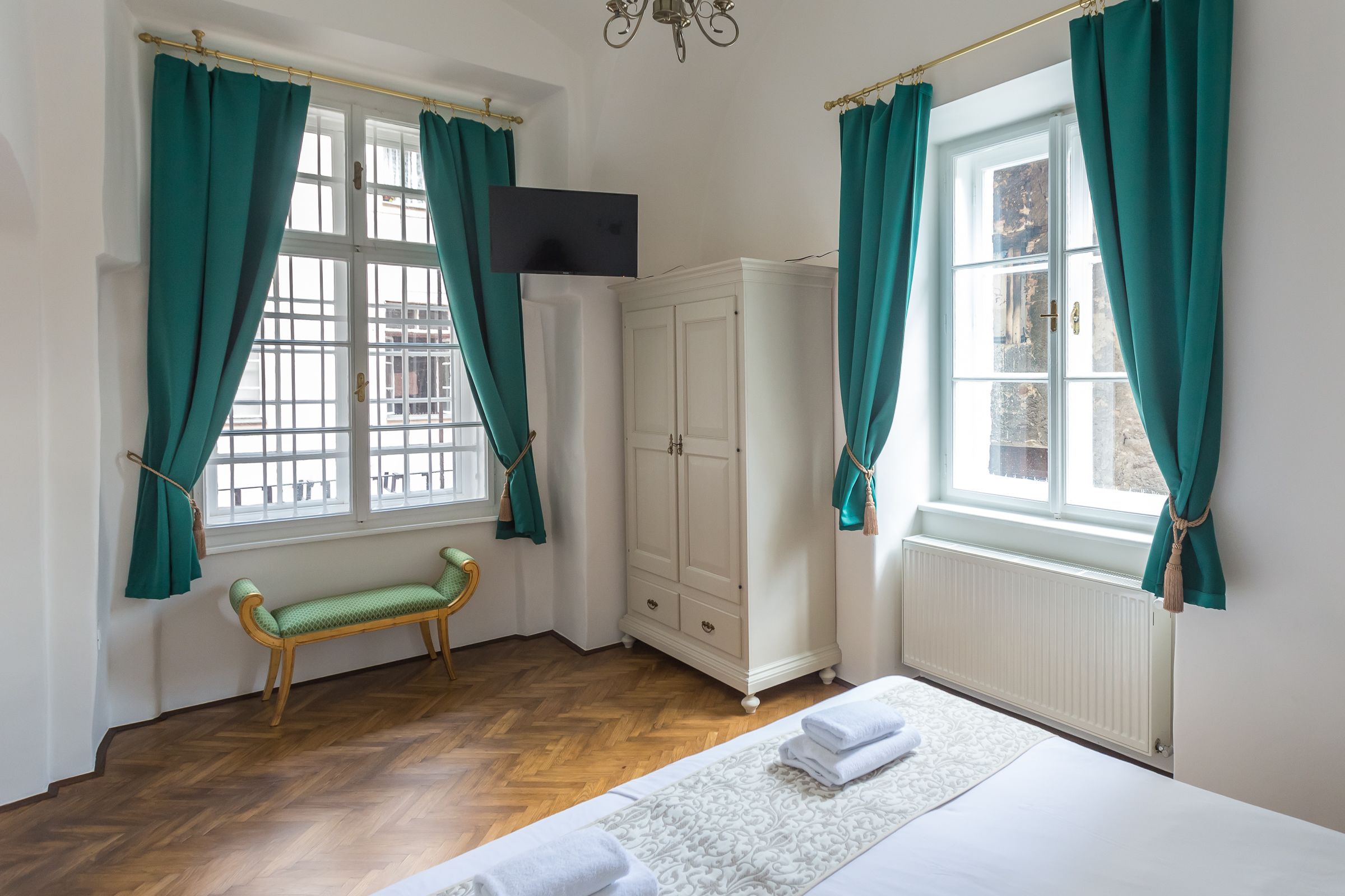 A room with a bed, a bench, a wardrobe, and a window with curtains.