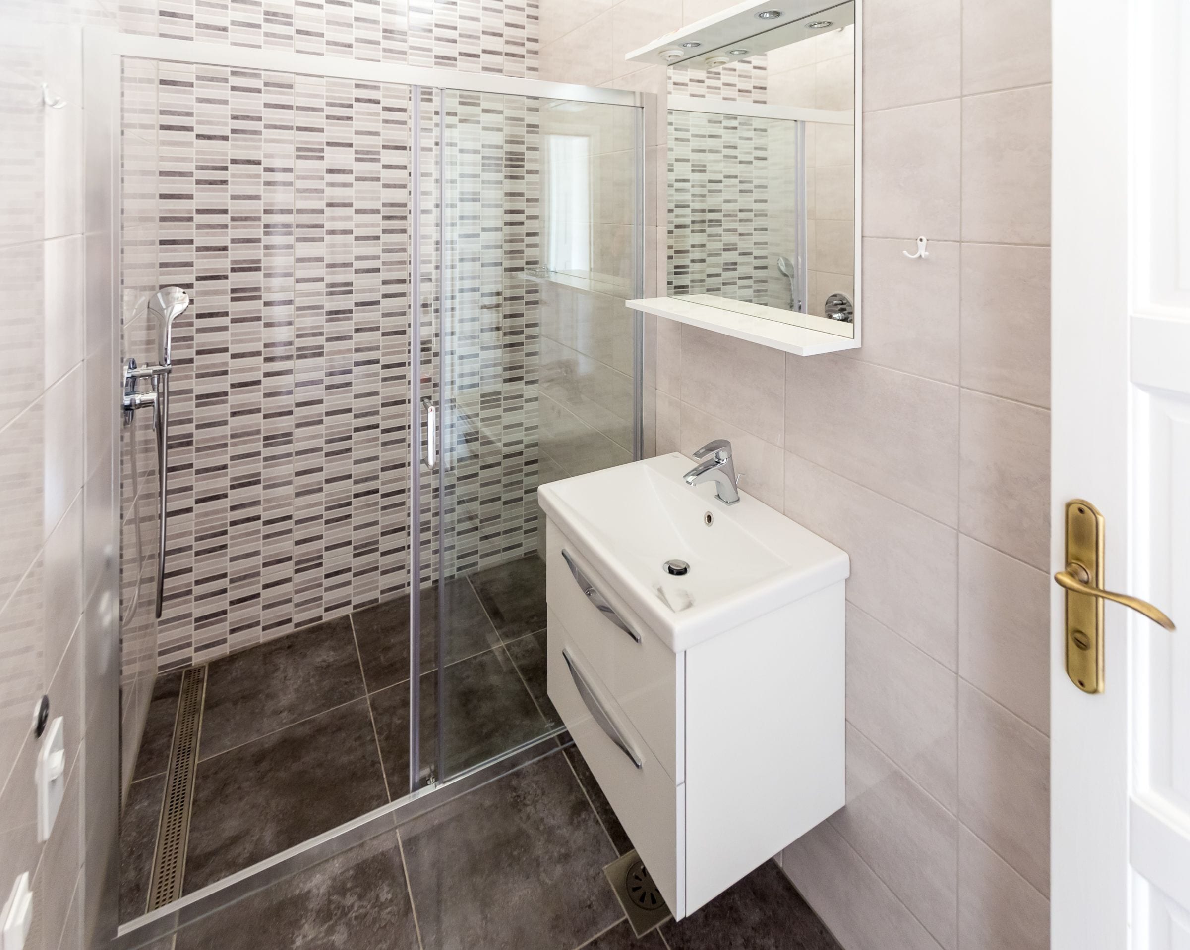 A modern bathroom with a glass shower enclosure, a white sink, and a mirror above it.