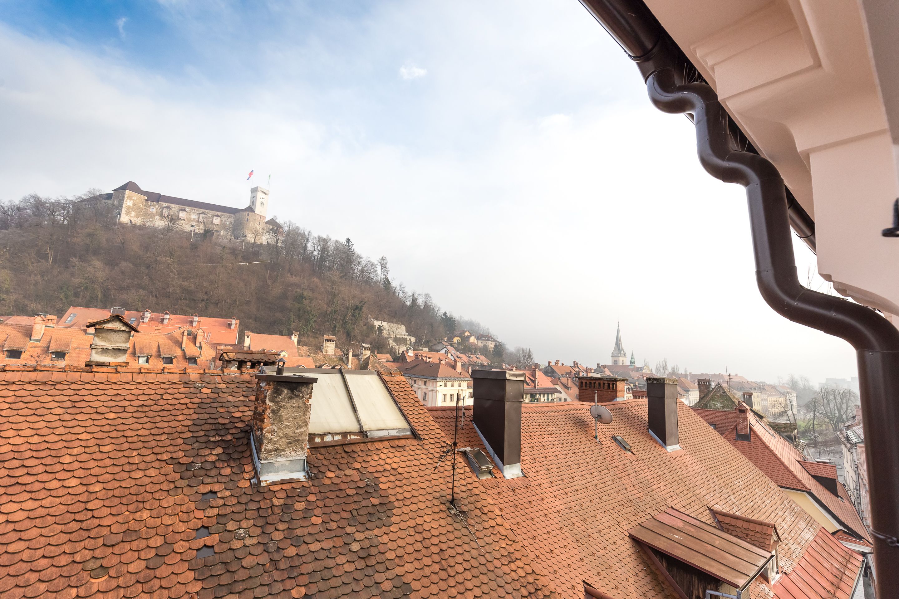 A view of a cityscape with a prominent hilltop building, terracotta-roofed buildings, and a clear sky.