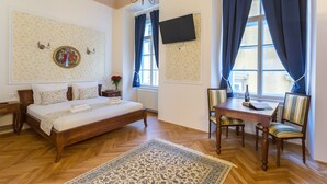 A hotel room with a bed, a desk with chairs, a chandelier, and a large window with curtains. - Barbo Palace (Ljubljana)