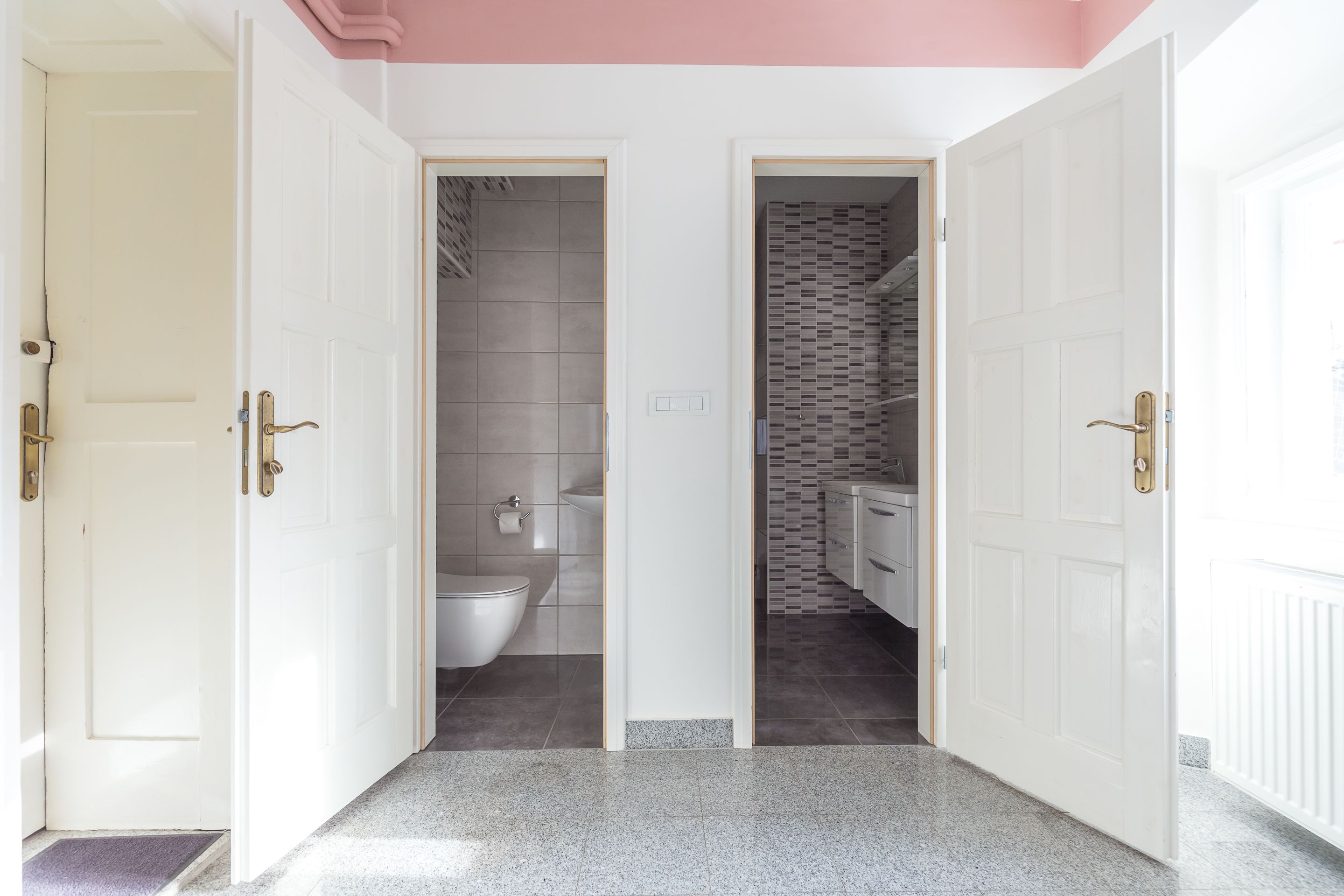 Een gang met twee geopende deuren die leiden naar een badkamer en een douchegedeelte.