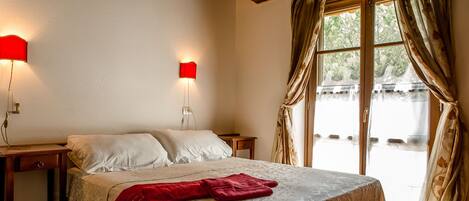 Un dormitorio con una cama grande, dos mesitas de noche y un ventanal con cortinas.