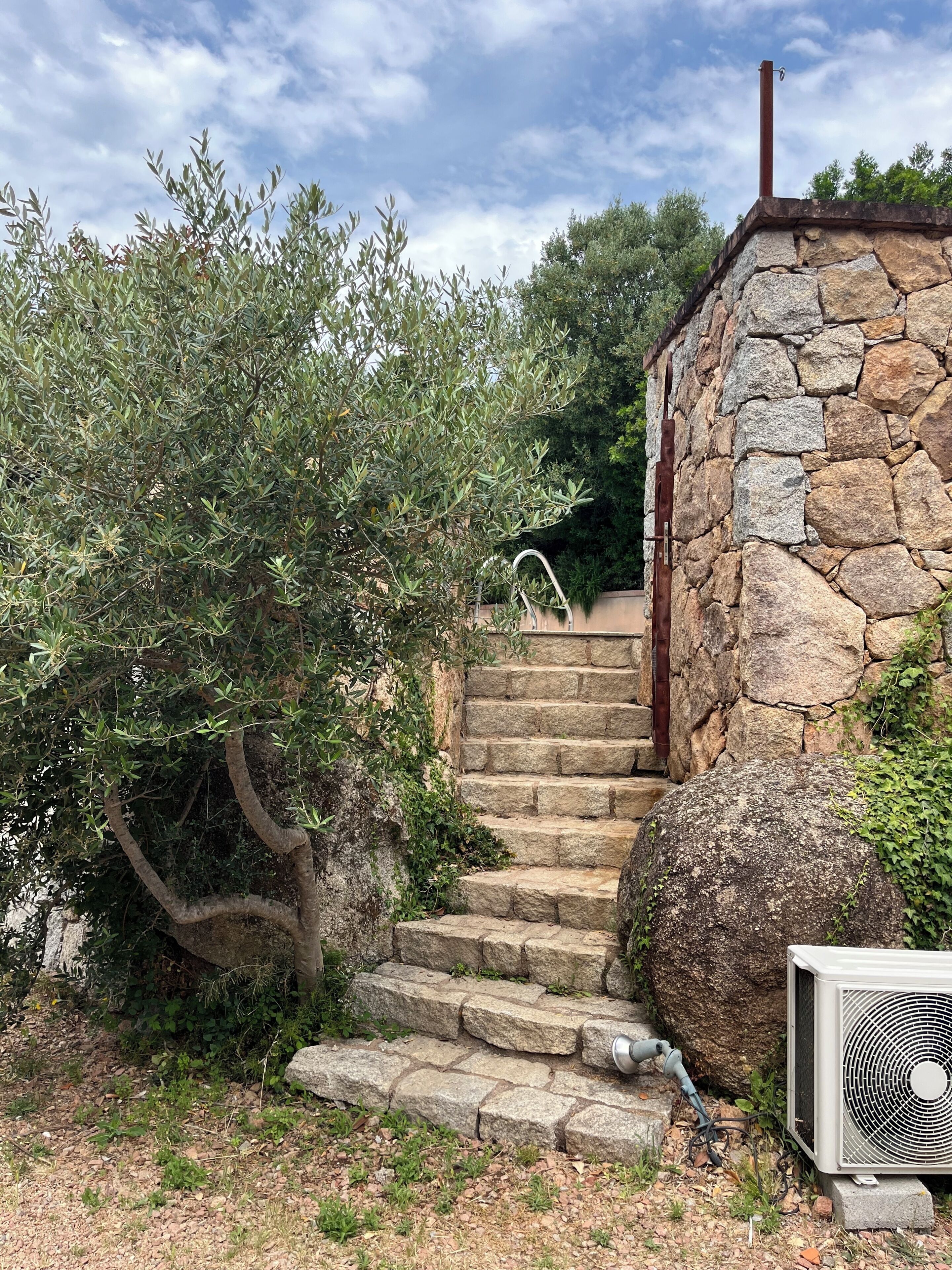 Stone steps leading to a stone wall with an air conditioning unit beside it.