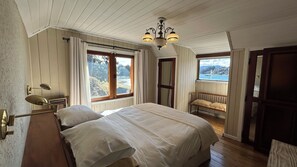 Un dormitorio con una cama grande, dos ventanas, un banco y una araña.