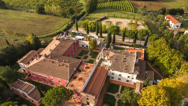 Vue aérienne d’un domaine viticole avec des champs en terrasses, un bâtiment principal à la façade rouge et un bâtiment plus petit, de couleur blanche.