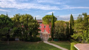 Un bâtiment rouge, doté d’une entrée fermée par un portail, entouré d’une végétation luxuriante et d’arbres.