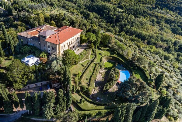 Vista aérea de una extensa propiedad con un edificio principal, una piscina y jardines cuidados.